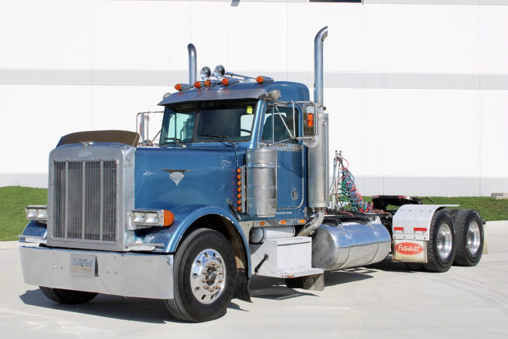 Used 1999 Peterbilt 379 Day Cab in metallic blue with dual exhaust stacks, chrome fuel tanks, and classic square headlights, featuring CAT 3406 engine and 15-speed manual transmission.