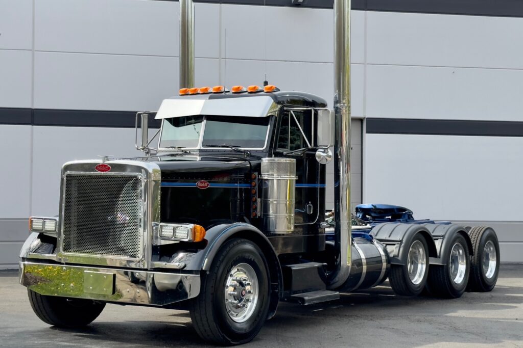 “Used 2004 Peterbilt 379 black tri-axle day cab with chrome dual stacks, aluminum fuel tanks, and a custom mesh grille , featuring CAT C15 diesel engine, 18-speed manual, and double wet kit with PTO.