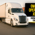Smiling truck driver with clipboard standing beside a white semi-truck and trailer in a freight yard , representing owner operator job opportunities and key information drivers should know before starting.