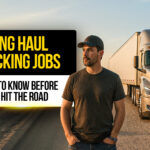 Truck driver standing on a rural highway in front of a silver semi-truck with a trailer , representing long haul trucking jobs and what drivers should know before getting started.
