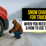 Truck driver installing snow chains on a red semi-truck tire in snowy mountain conditions, showing how and when to use tire chains for safe winter driving.